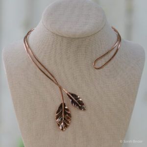 Asymmetrical copper neckwire with two leaves crisscrossing in front.